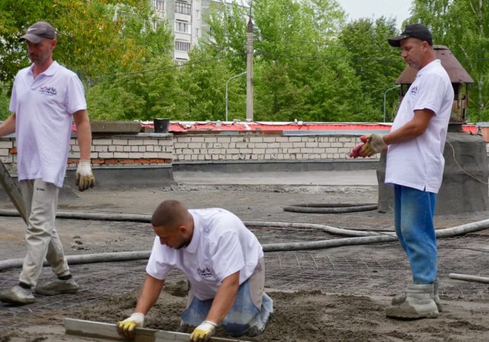 Team of construction workers pouring and leveling cement on a rooftop.