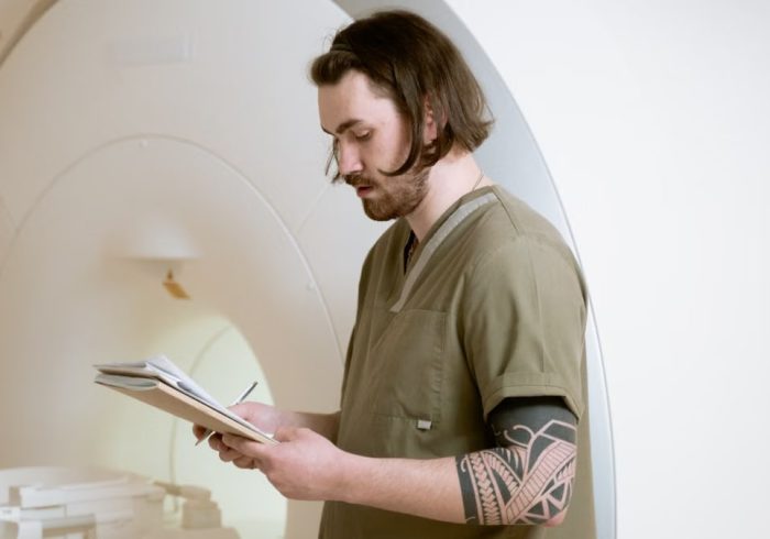 Radiology technician taking notes beside an MRI machine in a modern medical facility.