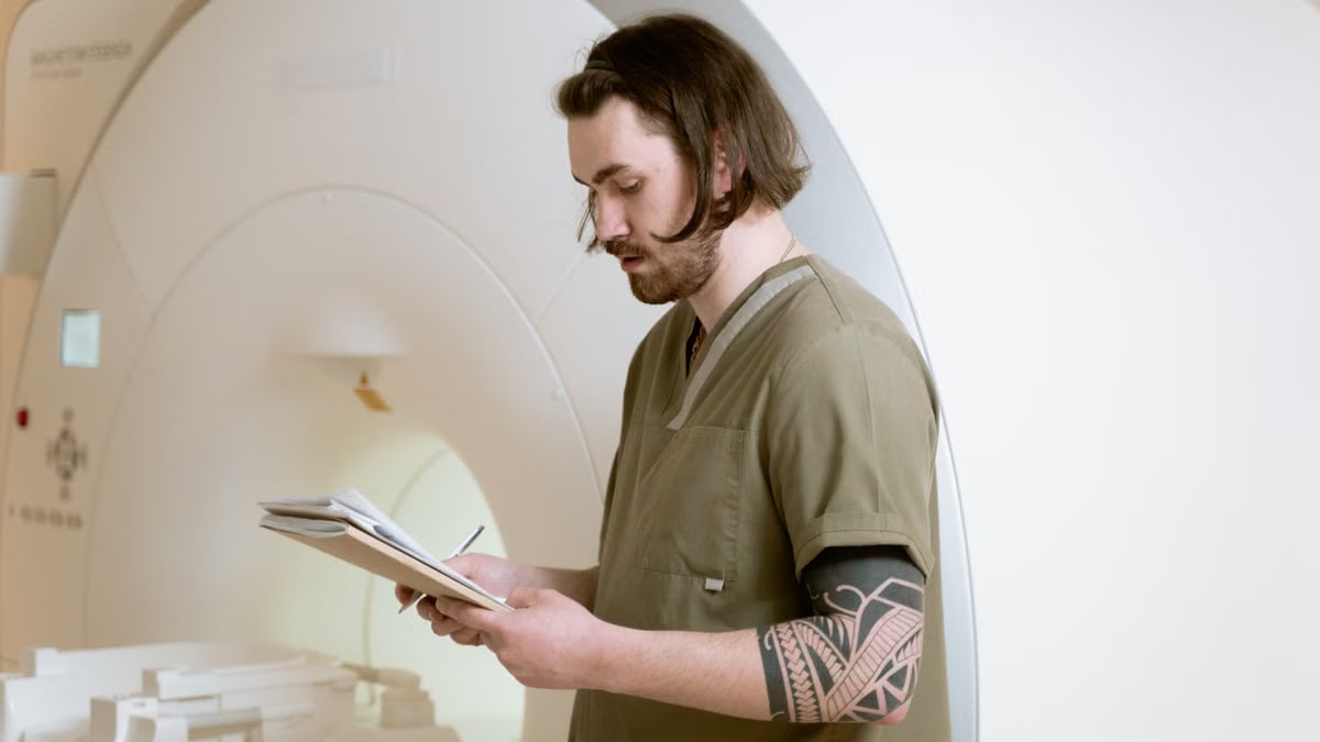 Radiology technician taking notes beside an MRI machine in a modern medical facility.