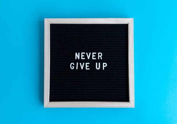 Black letter board with 'Never Give Up' message on a vibrant blue background.